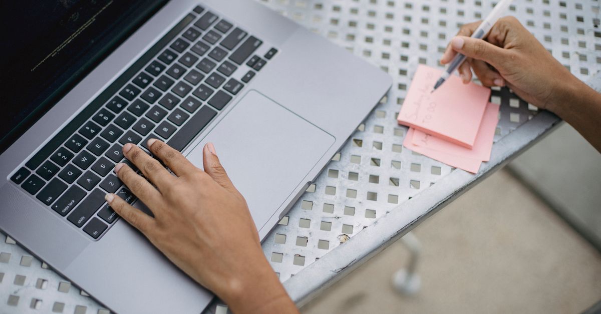 Close-up of a person using a laptop and writing notes at an outdoor workspace.